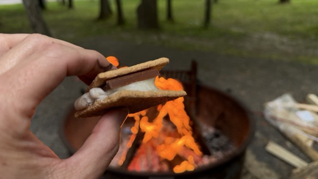 A finished s'more held up in front of the campfire